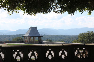 Built structure by trees and mountains against sky