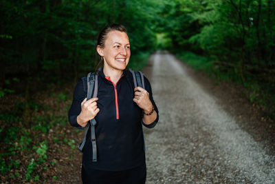 Smiling woman standing on road against trees