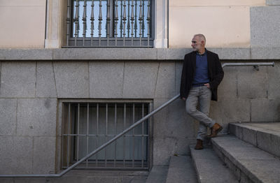 Adult man in suit standing on stairway in city against stone wall