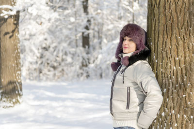 Portrait of young woman standing on tree trunk during winter