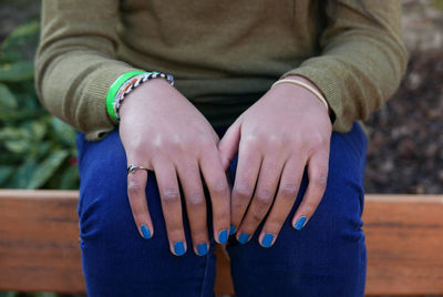 Midsection of woman with blue nail polish sitting on bench