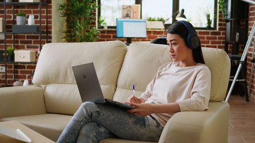 Young woman using laptop while sitting on sofa at home