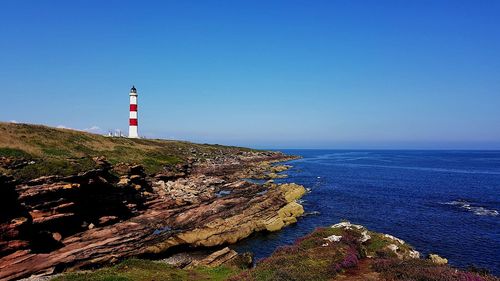 Lighthouse on beach by sea against sky