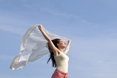 Low angle view of beautiful woman holding scarf against blue sky