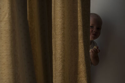Portrait of boy looking at camera from behind the curtain