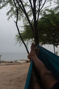 Young man relaxing on hammock by sea against sky