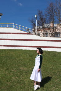 Side view of young woman looking away while standing on grassy field at park during sunny day