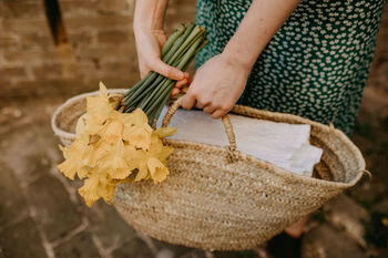 Midsection of woman holding bag and flowers