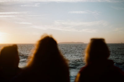 Low section of people at beach against sky during sunset