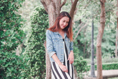 Young woman standing by tree trunk