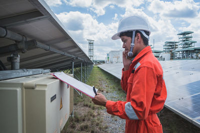 Side view of worker talking on phone while standing by solar panel