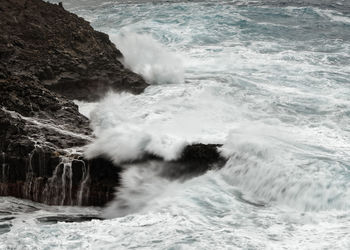 A wave breaks in stormy weather on a rocky coast with a small bay, canary islands, la palma