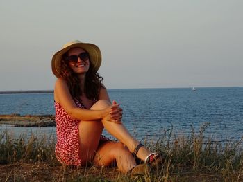 Portrait of smiling young woman sitting on beach against clear sky