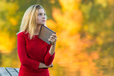 Young woman holding book while standing by bench in park