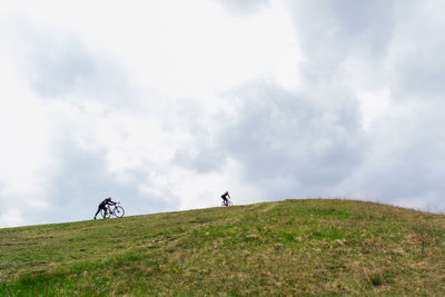 People riding bicycle on field against sky