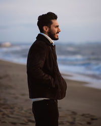 Side view of young man standing at beach against sky