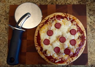 Directly above shot of pepperoni pizza with cutter on cutting board