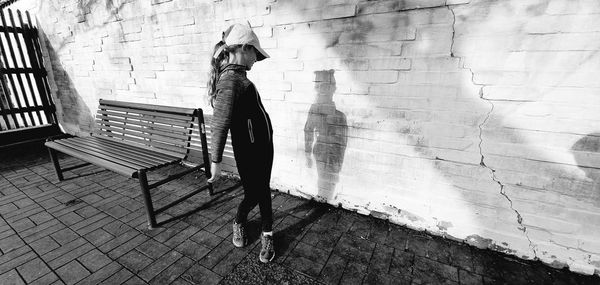 Rear view of woman standing on footpath against wall