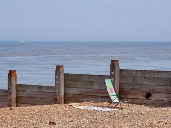 Wooden chairs on beach against sky