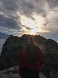 Young woman standing on rock against sky during sunset