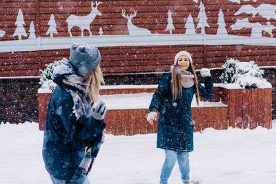 Two young women play snowballs and laugh while walking through a snowy town