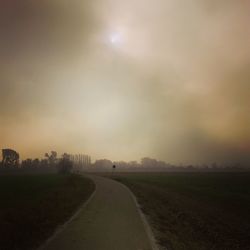 Road amidst field against sky during foggy weather