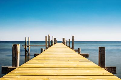 View of pier on sea against clear blue sky