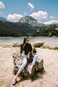 Portrait of young woman sitting on mountain against sky