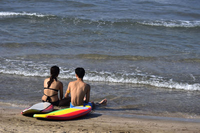 Rear view of couple sitting on shore at beach