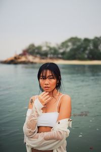 Portrait of beautiful woman standing by lake against sky
