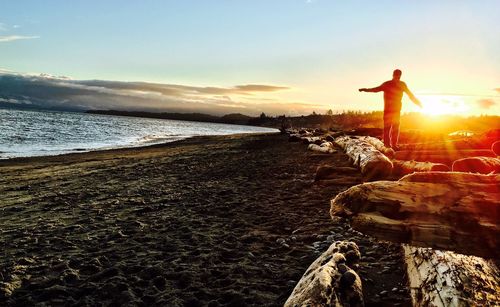 Man standing on rock at beach against sky during sunset