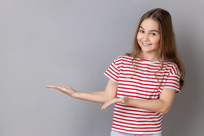 Portrait of young woman standing against gray background