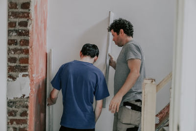 Two caucasian male plasterer man checks the evenness of the walls after puttying.