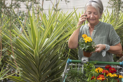 Senior woman talking on phone while standing amidst plant