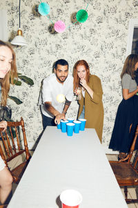 Confident young man playing beer pong on table by female friend at dinner party