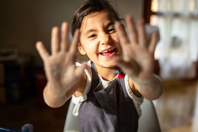 Girl with dark hair shows her hands dirty with flour