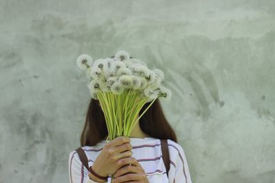 Mid adult woman holding flowers while standing against wall