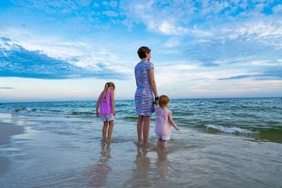 Rear view of siblings standing on beach against sky