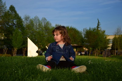 Cute girl sitting on grassy field against clear sky at park