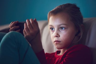 Close-up of girl with headphones using mobile phone while sitting on sofa at home