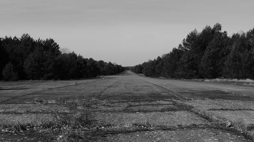 Dirt road amidst trees on field against clear sky