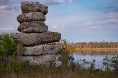 Stack of stones on rock by lake against sky