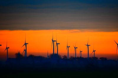 Silhouette wind turbines on field against romantic sky at sunset
