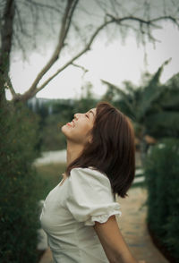 Side view of young woman looking away against trees