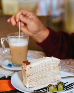 Close-up of hand of person with coffee and cake on table