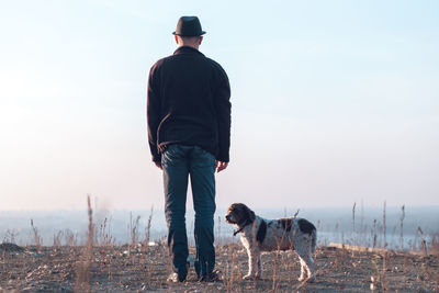 Rear view of man with dog on field against sky