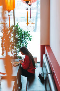 Beautiful smiling young asian woman in red clothes eating asian food with chopsticks in restaurant