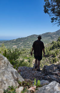 Rear view of man walking on mountain against clear sky