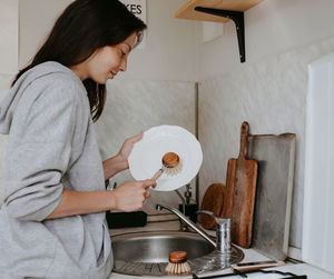 Side view of young woman washing dishes at home