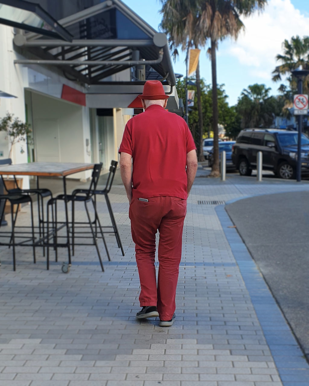 REAR VIEW OF MAN WALKING ON SIDEWALK IN CITY